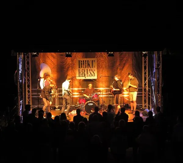 Duke Brass bei einem Konzert vor einer beleuchteten Bühnenwand